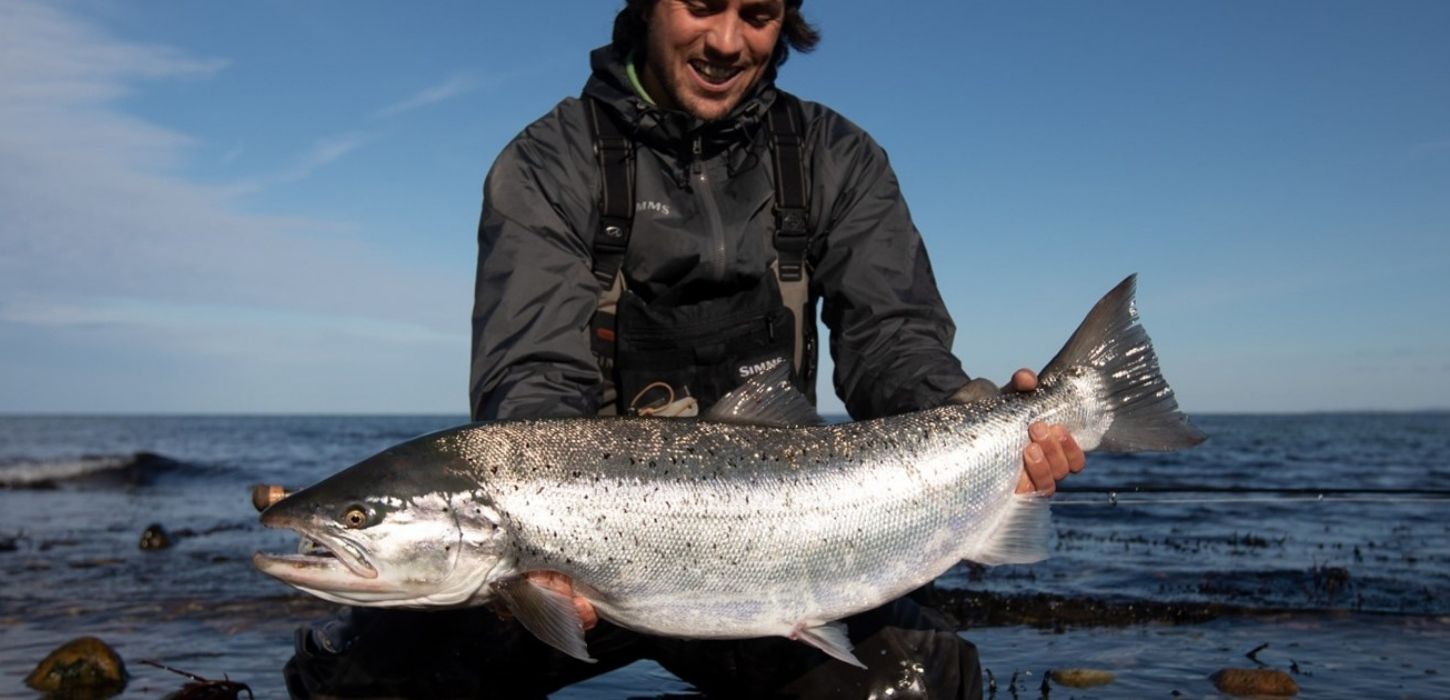 Ein Fischer mit einer Meerforelle in der Hand am Ufer