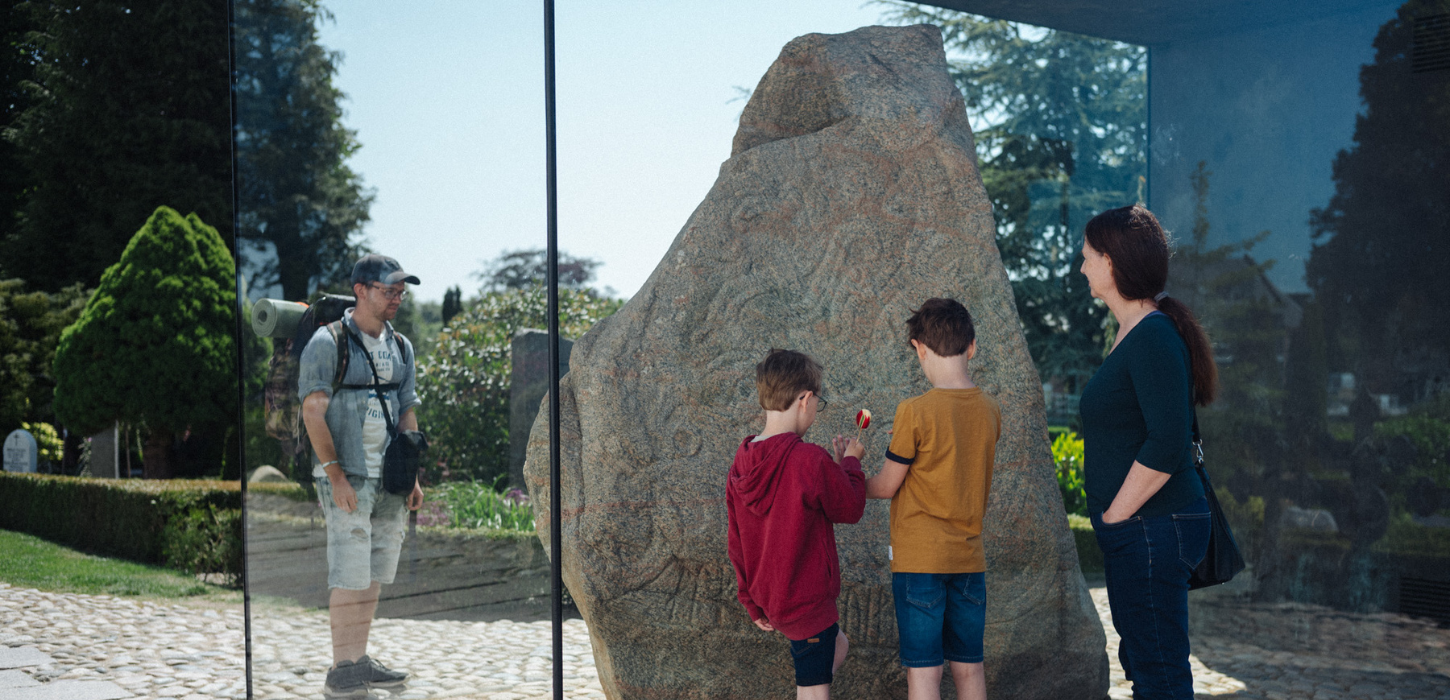 Familie kigger på den ene runesten ved monumenterne i Jelling