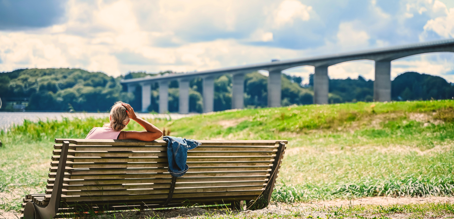En person sidder og nyder udsigten over Vejlefjordbroen fra en bænk ved Albuen Strand