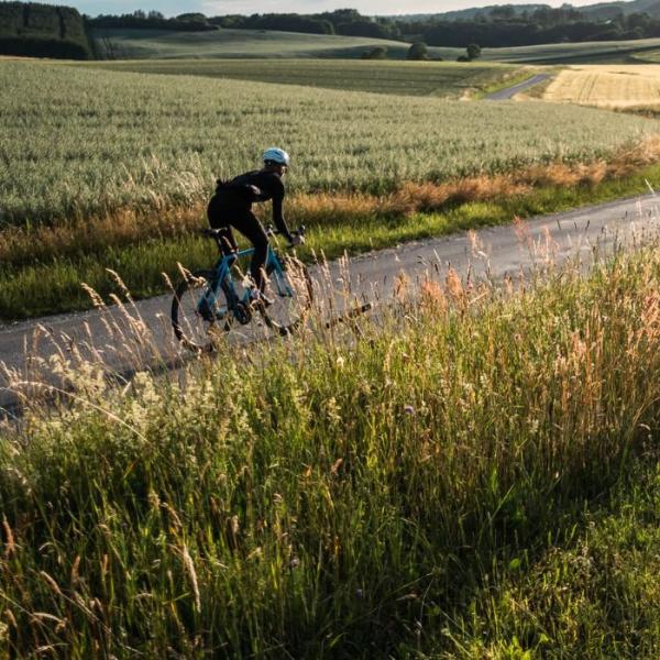 A person rides a racing bike on the country road along open fields in Vejle
