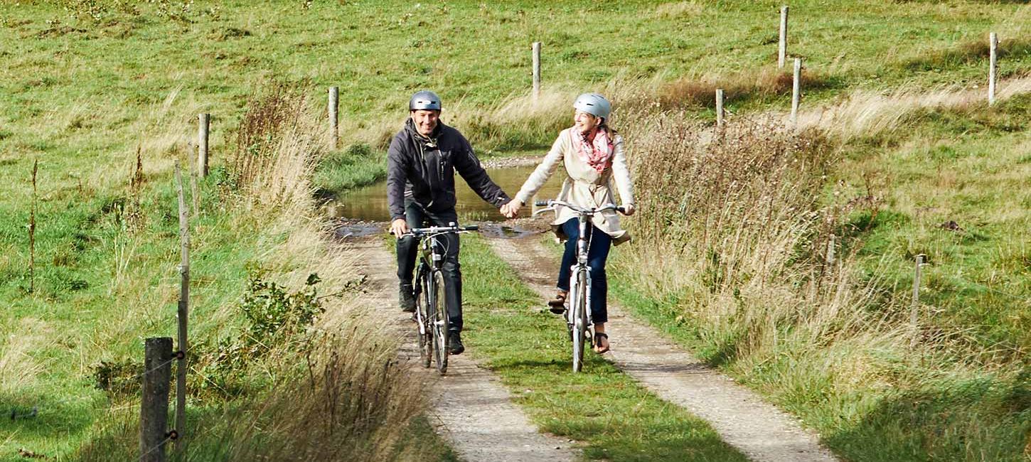 Two people on a bike ride along Hærvejen at Gudenåens Udspring cycle hand in hand on a spring day
