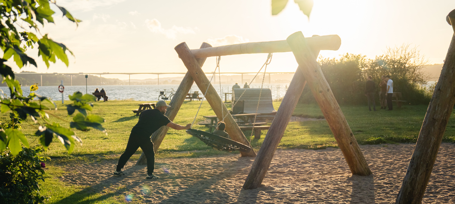 Father and child playing on a swing in the playground at Ibæk Beach