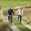 Two people on a bike ride along Hærvejen at Gudenåens Udspring cycle hand in hand on a spring day