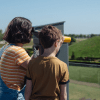 Two children look through binoculars from the roof terrace at Kongernes Jelling to the mounds