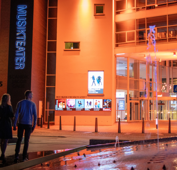 A couple on their way to Vejle Musikteater walks across the roundabout with the fountain out in front of the music theatre