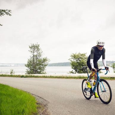 Road cyclists are heading up Munkebjergbakken. The Vejlefjord Bridge is visible in the background.