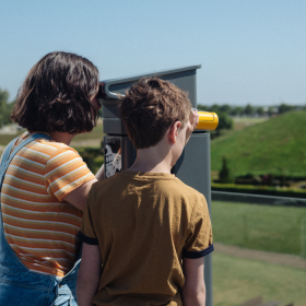 Two children look through binoculars from the roof terrace at Kongernes Jelling to the mounds
