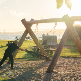 Father and child playing on a swing in the playground at Ibæk Beach