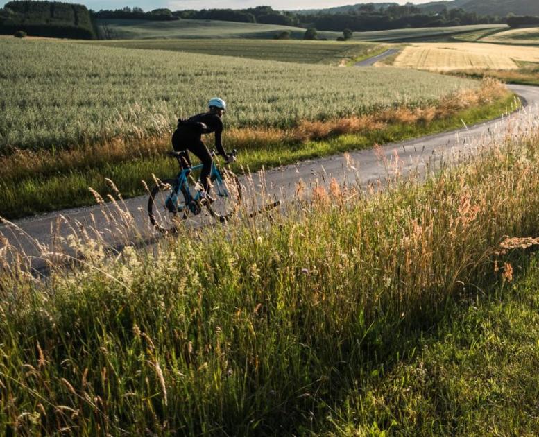 A person rides a racing bike on the country road along open fields in Vejle