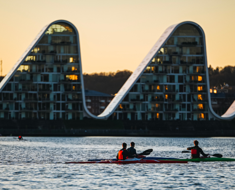 People in kayaks on Vejle Fjord with Bølgen (the Wave) in the background