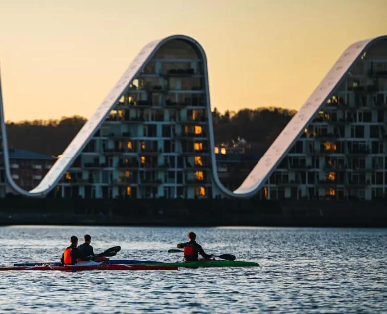 People in kayaks on Vejle Fjord with Bølgen (the Wave) in the background