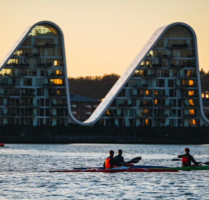 People in kayaks on Vejle Fjord with Bølgen (the Wave) in the background