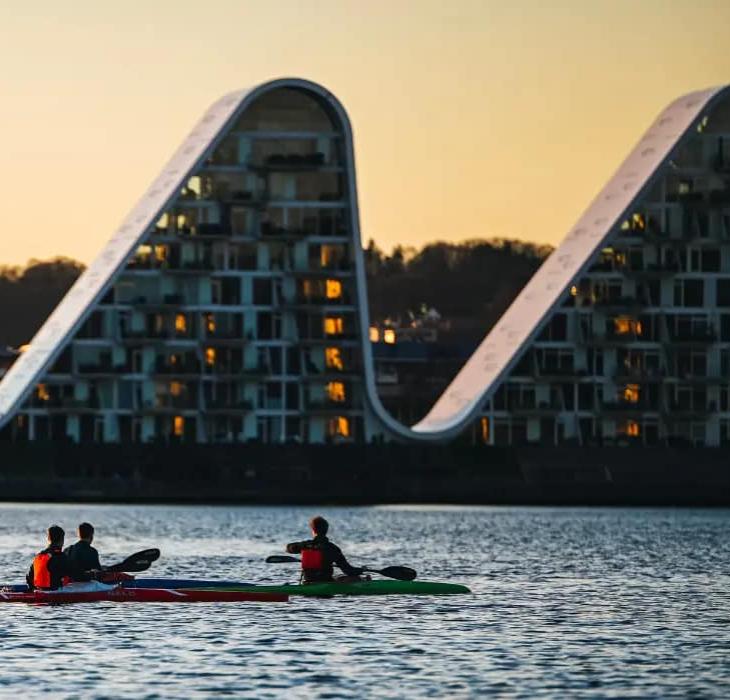 People in kayaks on Vejle Fjord with Bølgen (the Wave) in the background