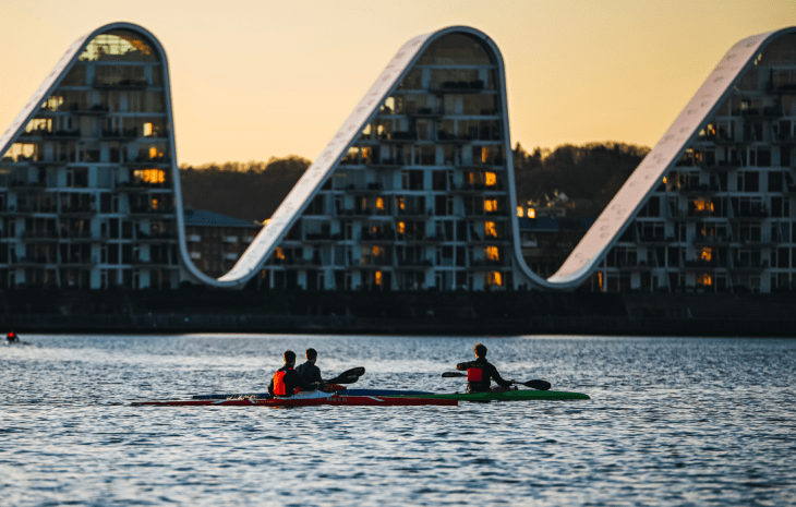 People in kayaks on Vejle Fjord with Bølgen (the Wave) in the background