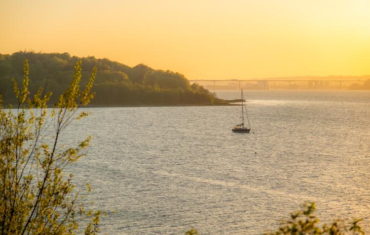 Vejle Fjord seen from Andkær Vig at sunset with a boat on the fjord and the Vejlefjord Bridge in the background